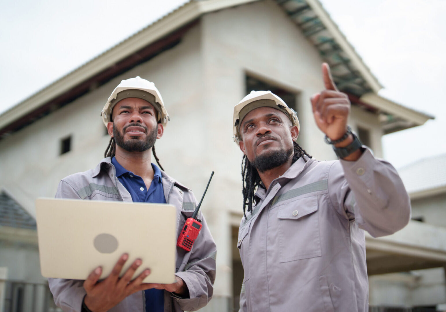Two construction workers inspecting house with laptop