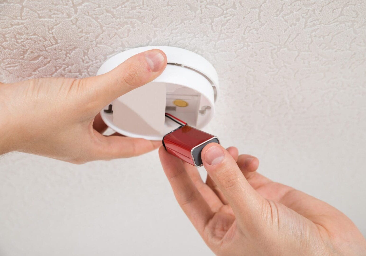 Hands replacing smoke alarm battery