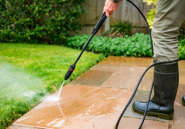Person pressure washing outdoor patio tiles.